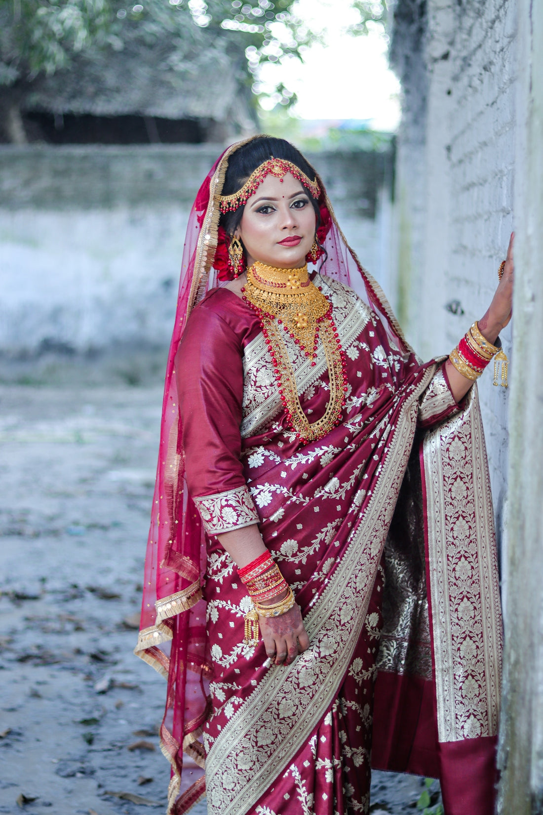 A bride in a maroon saree and gold jewelry