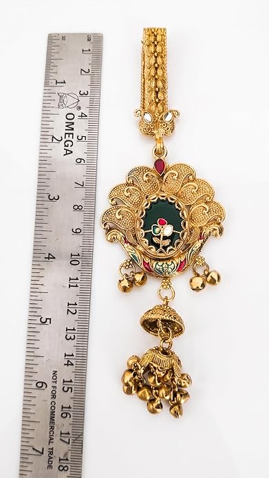 Gold pendant with intricate designs next to a ruler for scale on a white background