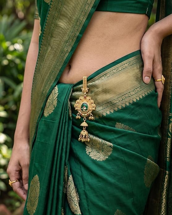 Green saree with gold embroidery and a decorative pendant, worn by a person.