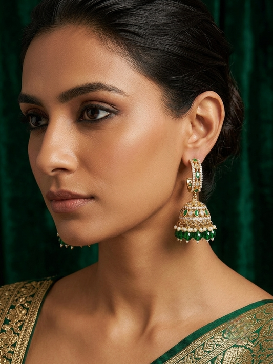 Close-up profile of a female model wearing statement gold-toned emerald green hoop jhumka earrings paired with a green and gold embroidered ethnic outfit.