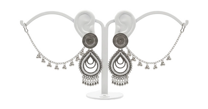 A pair of silver-toned traditional Indian dangle earrings displayed on a white ear-shaped jewelry stand against a clean white background.