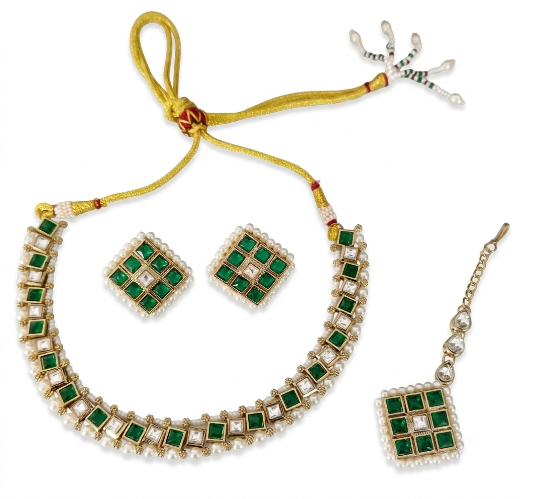 Angled flat lay of a complete artificial Kundan jewelry set including a choker necklace, matching square earrings, and a maang tikka, featuring emerald green stones and pure white pearl borders with a gold adjustable dori.