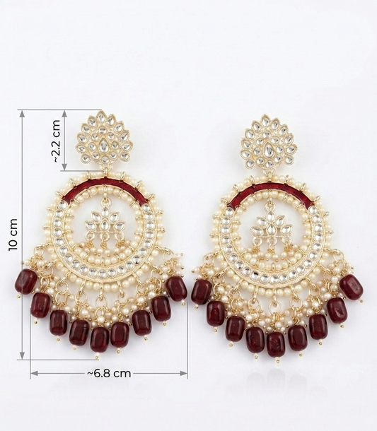 A pair of gold-toned Indian chandelier earrings with white faux pearls, red enamel accents, and dangling dark red beads, shown with dimension lines indicating measurements of 10 cm height, 2.2 cm stud-to-circle distance, and 6.