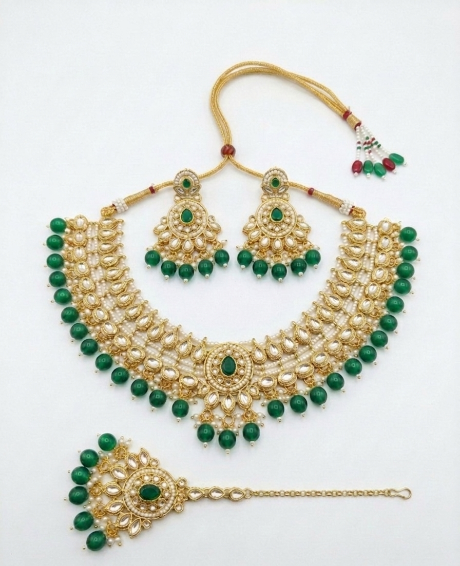 Gold-toned traditional Indian jewelry set with a necklace, matching earrings, and a maang tikka, decorated with green beads and stones on a plain white background.