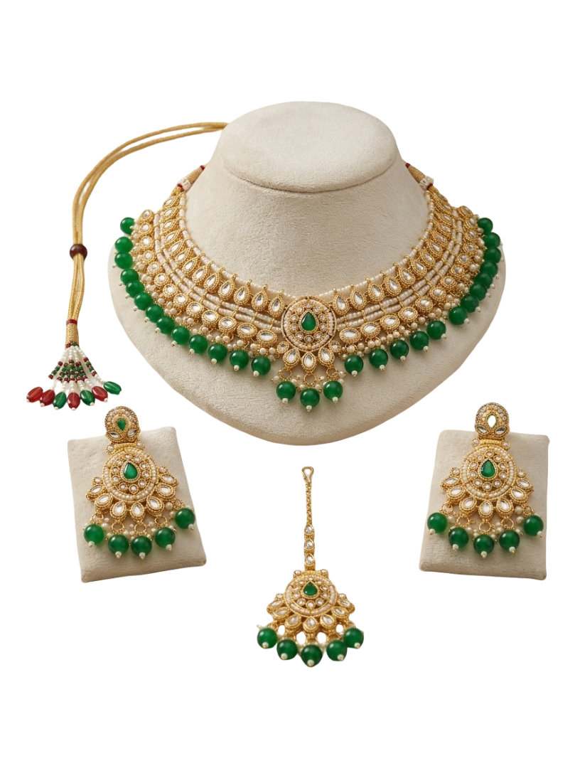Gold-toned traditional Indian jewelry set featuring a choker necklace, matching earrings, and a maang tikka, decorated with faux pearls, green stones, and red accents, displayed on a cream-colored mannequin bust and individual stands against a white background.